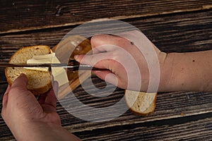 Someone spreads a little butter with a knife on fresh wheat toast, a piece of butter in a wooden butter dish, and fresh