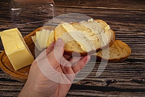 Someone spreads a little butter with a knife on fresh wheat toast, a piece of butter in a wooden butter dish, and fresh wheat