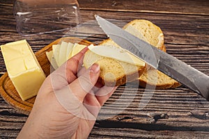 Someone spreads a little butter with a knife on fresh wheat toast, a piece of butter in a wooden butter dish, and fresh wheat