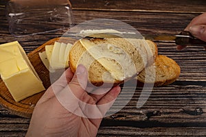 Someone spreads a little butter with a knife on fresh wheat toast, a piece of butter in a wooden butter dish, and fresh wheat