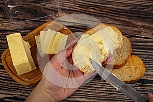 Someone spreads a little butter with a knife on fresh wheat toast, a piece of butter in a wooden butter dish, and fresh wheat