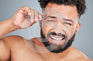 Somethings have just gotta be done. Studio portrait of a handsome young man tweezing his eyebrows against a grey