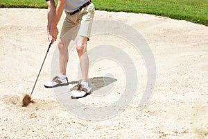 Sometimes golfing gets a little tricky. Senior man trying to hit his ball out of the sandtrap on the golf course.