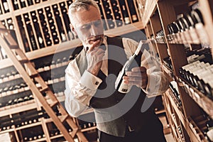 Sommelier Concept. Senior man standing reading label on bottle of wine curious