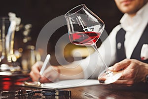 Sommelier fills form describing taste of red wine at table. Degustation of alcoholic beverages.