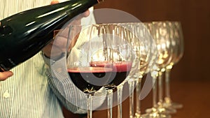 Sommelier hand pouring red wine into a row of crystal glasses