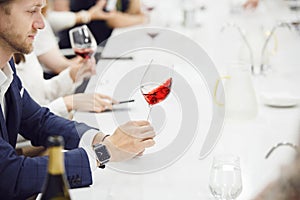 Sommelier holding wine glass and evaluates the appearance of red wine, looking at color, clarity, astringency and photo