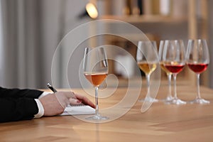 Sommelier making notes during wine tasting at table indoors, closeup