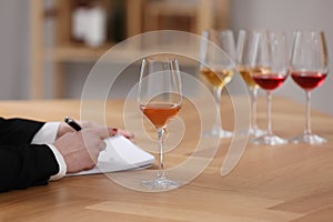 Sommelier making notes during wine tasting at table indoors, closeup