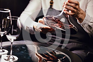 Sommelier pouring red wine from bottle into decanter at table in restaurant