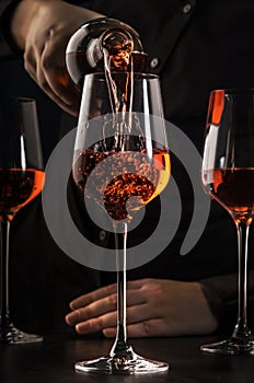 Sommelier pouring rose wine into glass at wine tasting in winery, bar or restaurant. Dark background photo