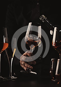 Sommelier pouring rose wine into glass at wine tasting in winery, bar or restaurant. Black toned image
