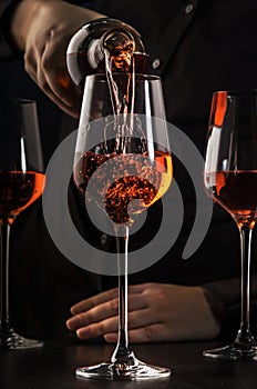 Sommelier pouring rose wine into glass at wine tasting in winery, bar or restaurant. Dark background