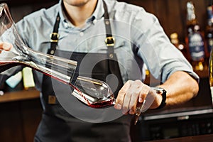 Sommelier pouring wine into glass from mixing bowl. Male waiter