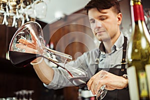 Sommelier pouring wine into glass from mixing bowl. Male waiter