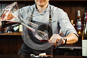 Sommelier pouring wine into glass from mixing bowl. Male waiter