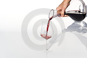 Sommelier pours red wine from decanter to wineglass on white background.