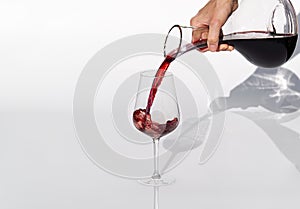 Sommelier pours red wine from decanter to wineglass on white background.