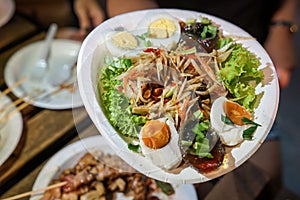 Somtum; Spicy papaya salad with pickled fish in paper dish at foodtruck street food event., Bangkok, Thailand