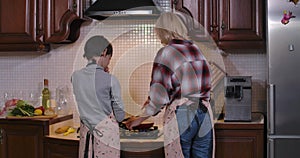 Son burning hand helping mother with cooking. Back view of Caucasian woman and boy preparing dinner in kitchen at home