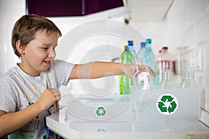 Son child sorts plastic for recycling in the kitchen at home. A child helps his mother sort plastic into boxes