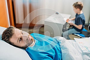 Son drawing pictures while sick father laying on hospital bed at ward