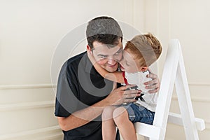 The son embraces the beloved daddy. Little boy is sitting on a step-ladder