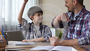 Son and father doing homework together, giving high five each other, teamwork