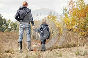 Son and father with full basket of mushrooms on the forest glade