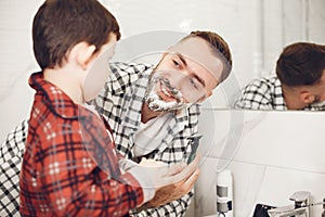 Son and father shaving in bathroom mirror