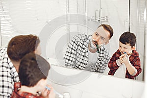 Son and father shaving in bathroom mirror