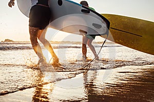 Son and father surfers run in ocean waves with surfing boards