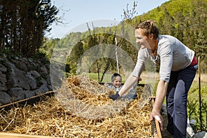 Son helping mother layering straw mulch in a raised garden bed