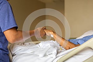 Son holding father is hand in bed in hospital