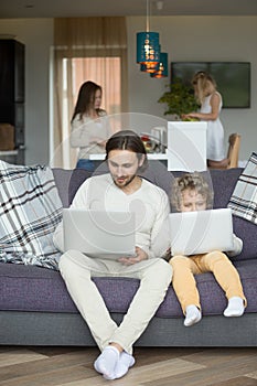 Son imitating father sitting on couch holding laptop at home