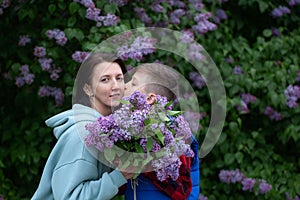 Son kisses his mother and gives her a bouquet of lilacs. Mother and son hugging, mother`s love
