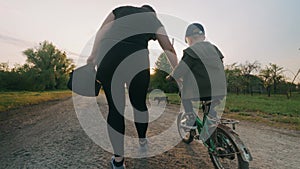 The son learns to ride a bicycle on the street with his mother.