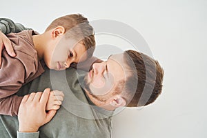 The son lies on the shoulder of his father. Dad hugs his child and smiles. Child care.