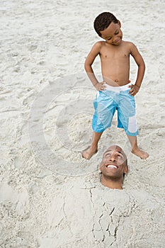 Son looking at father buried in sand