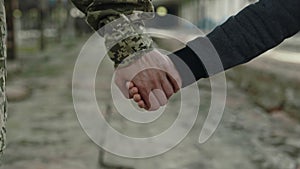 Son and military mother holding hands among old plant