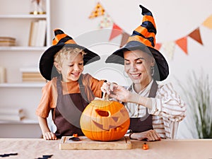 Son and mom making Jack-o-Lantern together at home, carving Halloween pumpkin