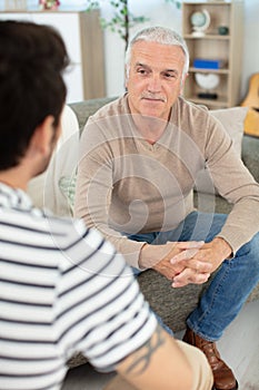 son and senior father sitting on sofa indoors at home