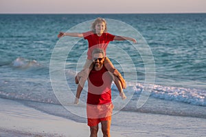 Son sits on fathers shoulders piggyback ride. Father and son walk in sea beach. Concept of friendly family. Dad with kid