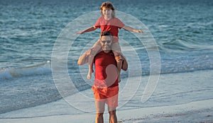 Son sits on fathers shoulders piggyback ride. Father and son walking together on the beach. Fatherhood family concept