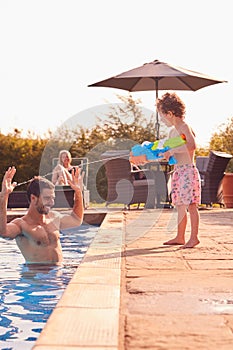 Son Squirting Father With Water Pistol Playing In Swimming Pool On Summer Vacation photo