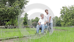 The son took his father who was sitting in a wheelchair. Take a walk in the fresh air in an outdoor park.