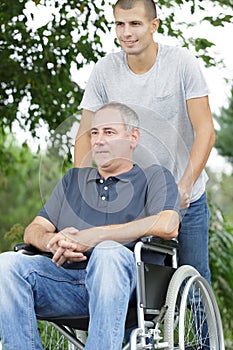 Son walking with disabled father in wheelchair at park