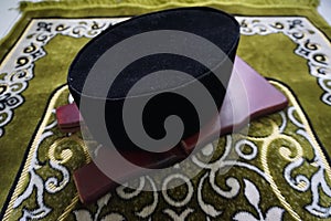 Songkok and book rest on the top of green prayer mat photo