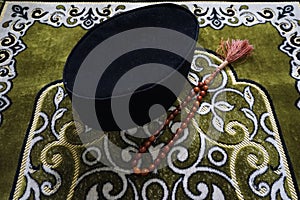 Songkok and brown color rosary on the top of green prayer mat photo