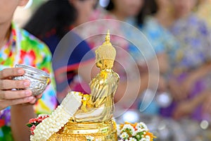 Songkran festival, Thai New Year. female hand holding silver bowl pouring water with jasmine and roses onto buddha statue